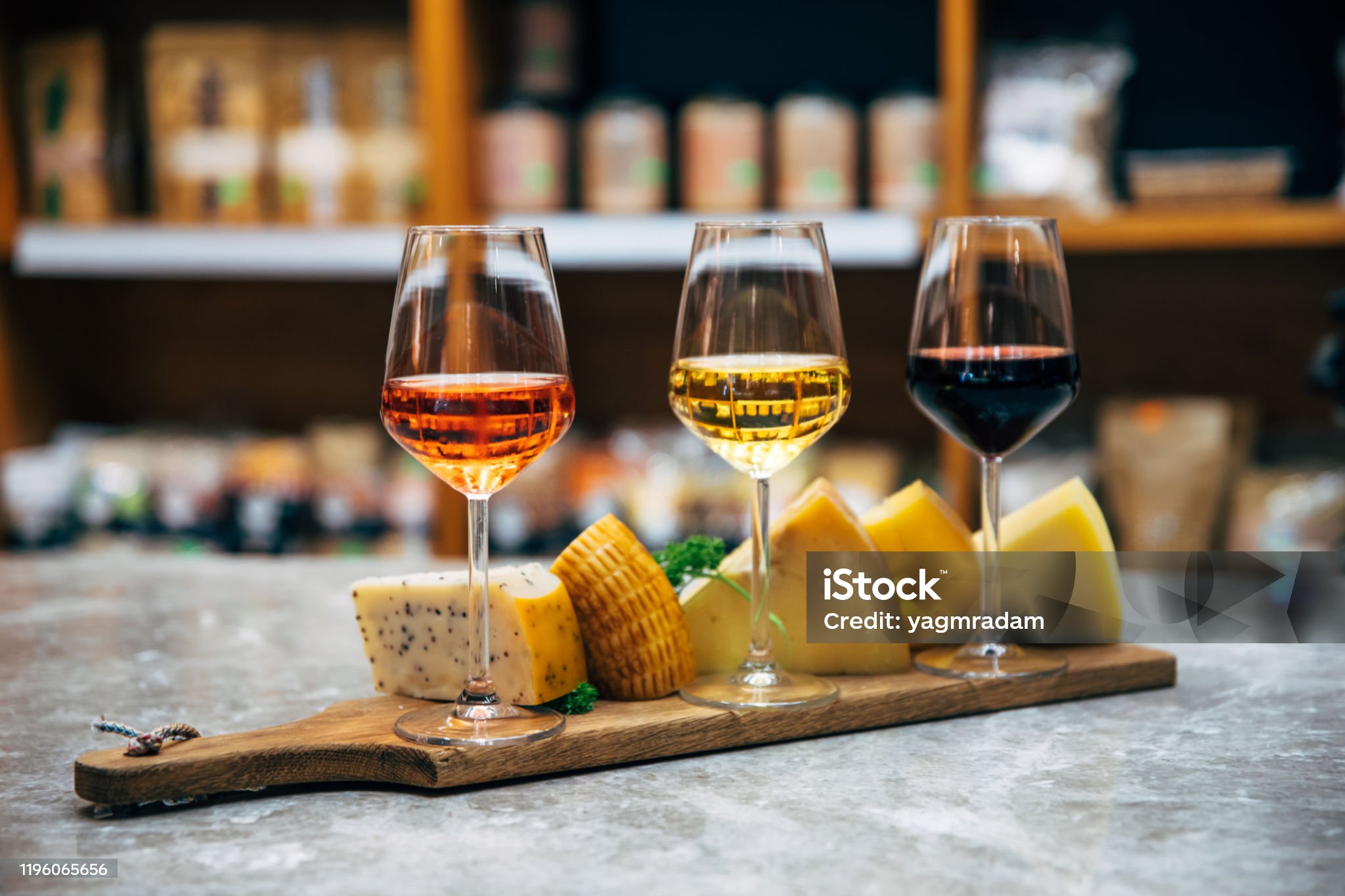 손잡이가 있는 평편한 나무 위에 몇개의 치즈 조각과 3개의 유리잔에 빨간색 노란색 주황색 와인이 담긴 사진입니다.