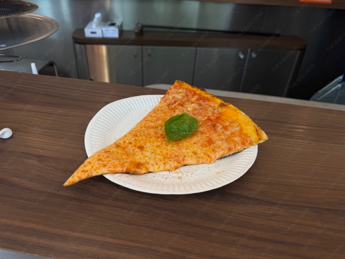 A crispy slice of Margherita pizza with a fresh basil leaf on a white paper plate