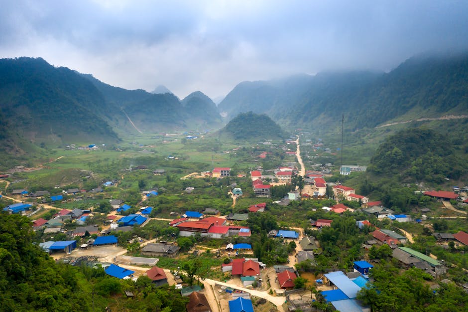 A scenic aerial view of a village nestled within lush green mountains under an overcast sky.
