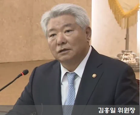 김홍일 위원장이 양복을 입고 마이크에 대고 말하는 사진