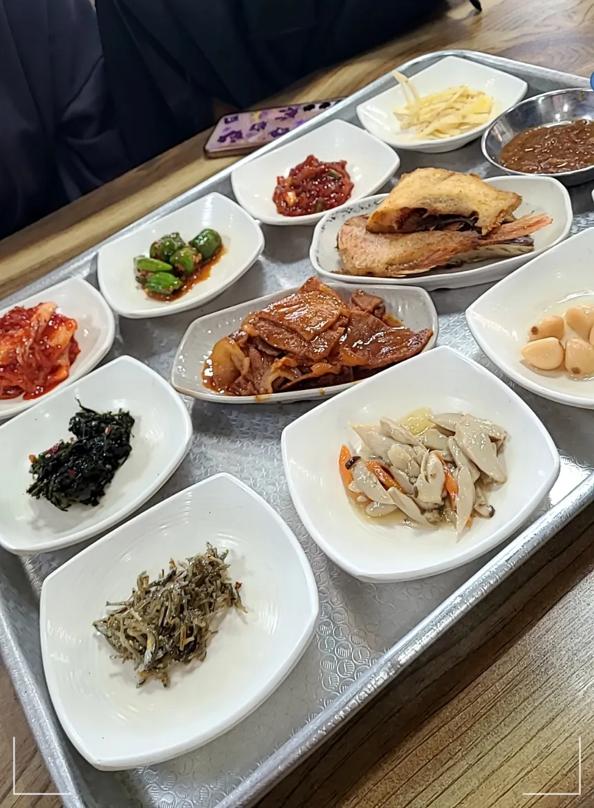 나무테이블 네모난 은쟁반 안에 열기구이 돼지고기볶음 고추무침 오징어젓갈 쌈장 감자채볶음