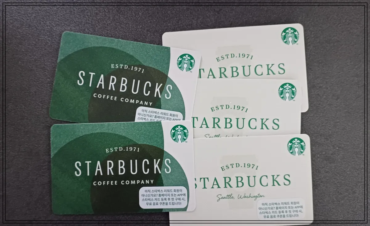 검은색-식탁위에-스타벅스-기프트카드-5장-2장은-초록색-바탕에-흰식으로-스타벅스라고-영어로-쓰였고-3장은-흰색바탕에-초록색으로-영어로-스타벅스라고-쓰임