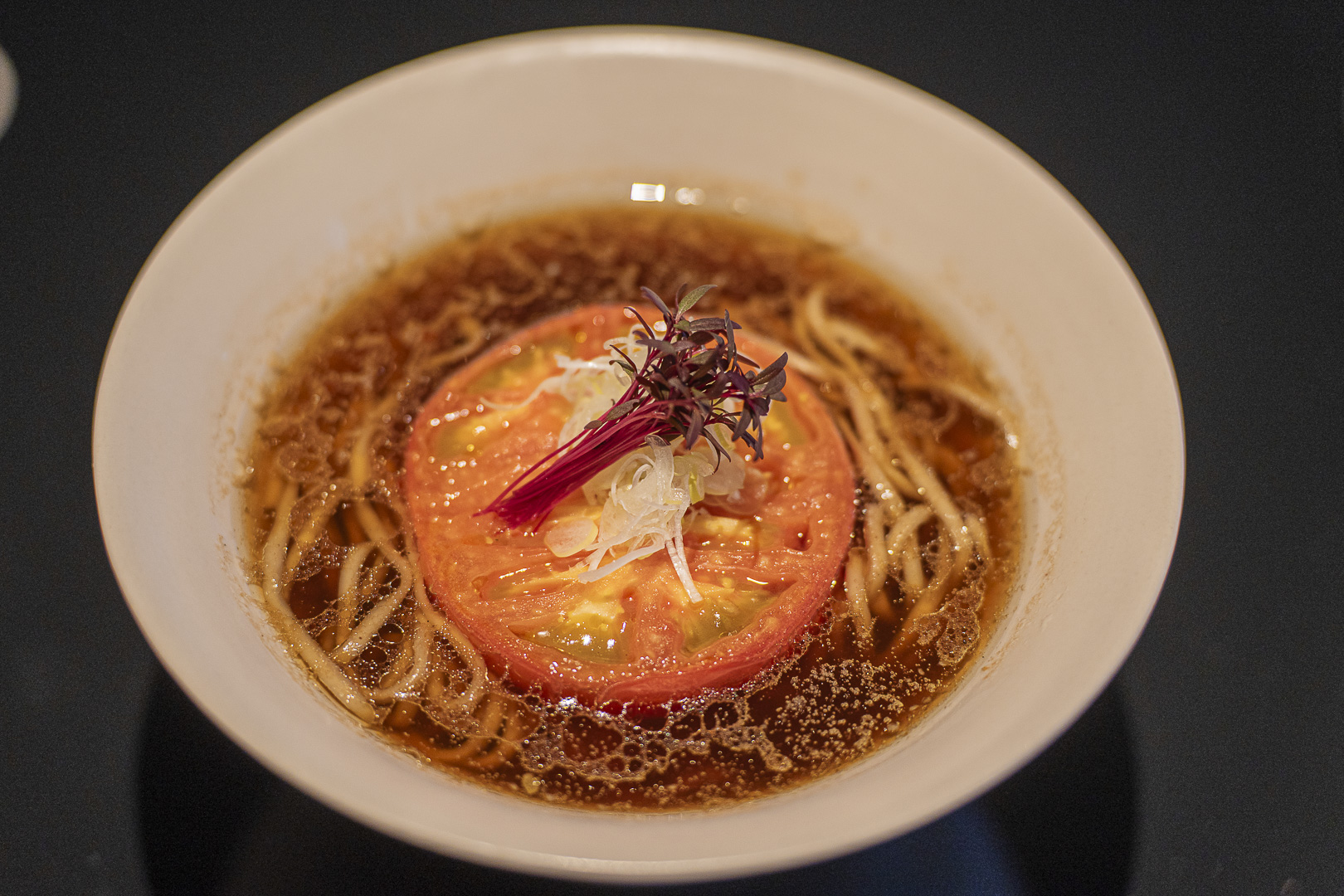 Vegan Ramen UZU Kyoto: ramen in brown broth topped with a broad slice of tomato and vegetables.