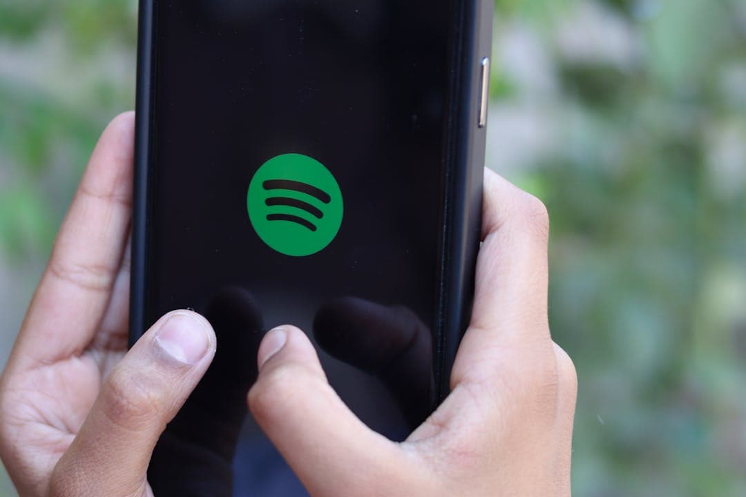 스포티파이 로고가 보이는 스마트폰 화면을 손으로 터치하는 장면