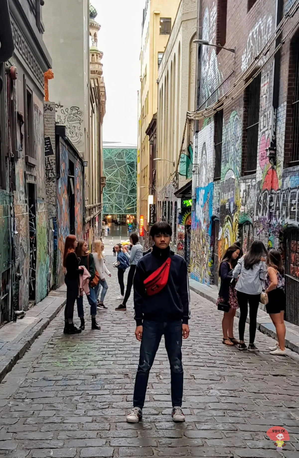 호주-멜버른-호시어-레인-거리-입구-벽을따라-이어지는-그래피티-사이에서-빨간-힙색을-매고-정면포즈-취하는-소년