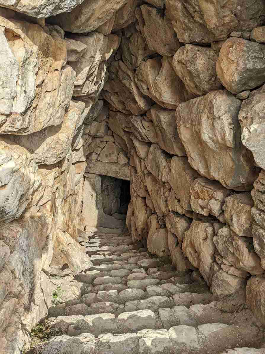 미케네 유적지의 비밀 지하통로 안쪽에서 어둡고 깊은 계단과 두꺼운 바위 벽이 보인다.