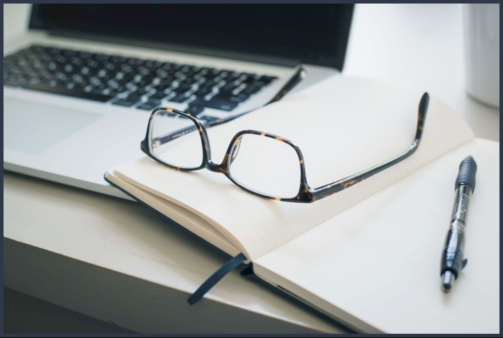 노트북과 공책 위 안경과 볼펜