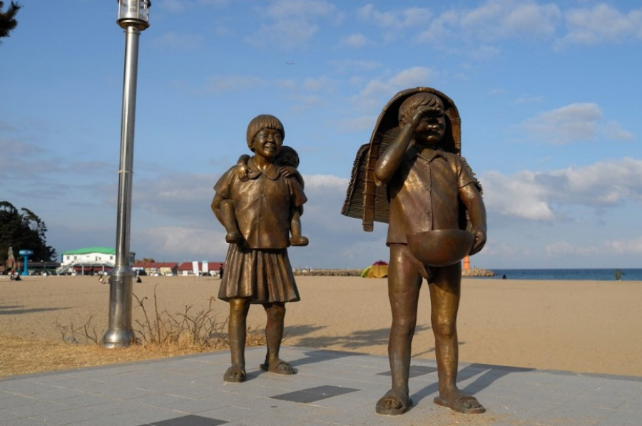 밤에 이불에 오줌을 싼 어린 아이가 머리에 키를 쓰고 바구니를 들고 울고 있고, 그 뒤에는 동생을 업은 누나가 웃으며 따라 오고 있는 것을 동상으로 만든 것을 찍은 사진