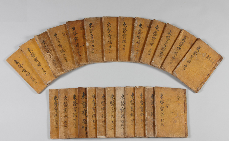 동의보감 옛고서를 하얀 바닥 위에 위에는 13권을 부채꼴 모양으로 놓아두고, 밑에는 12권을 가로로 포개어 놓아둔 것을 찍은 사진