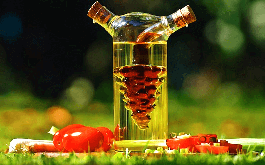 투명한 유리병에 현미식초가 가득 들어있다. 병 앞에는 빨간 방울토마토들이 있다.