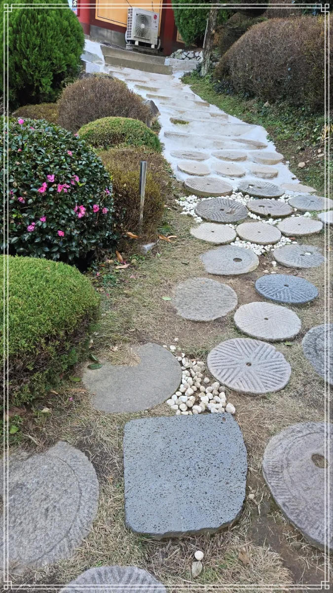 창원-장수암-전각과-전각을-통하는-사잇길-바닥에-분해된-맷돌을-디딤용-발판으로-바닥에-여러개-깔아놓았고-동백꽃-나무도-길-옆에-피어있다