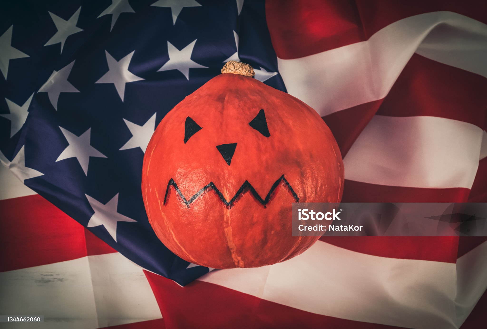 미국 성조기 국기앞에 빨간색 호박에다가 세모난 눈코 그리고 입을 그려넣은 사진입니다.