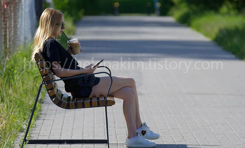 벤치에 앉아 물을 마시며 잠시 쉬고 있는 여자 이미지.