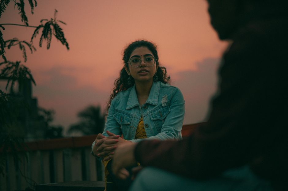 Young woman in denim jacket with eyeglasses during a sunset conversation outdoors.