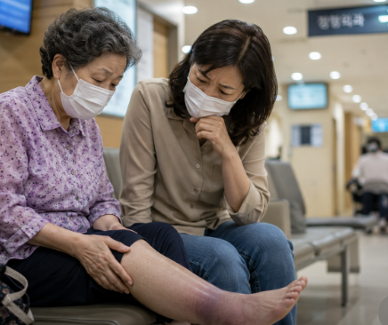 병원 대기실에서 어머니의 부은 발을 걱정스럽게 바라보는 딸의 모습