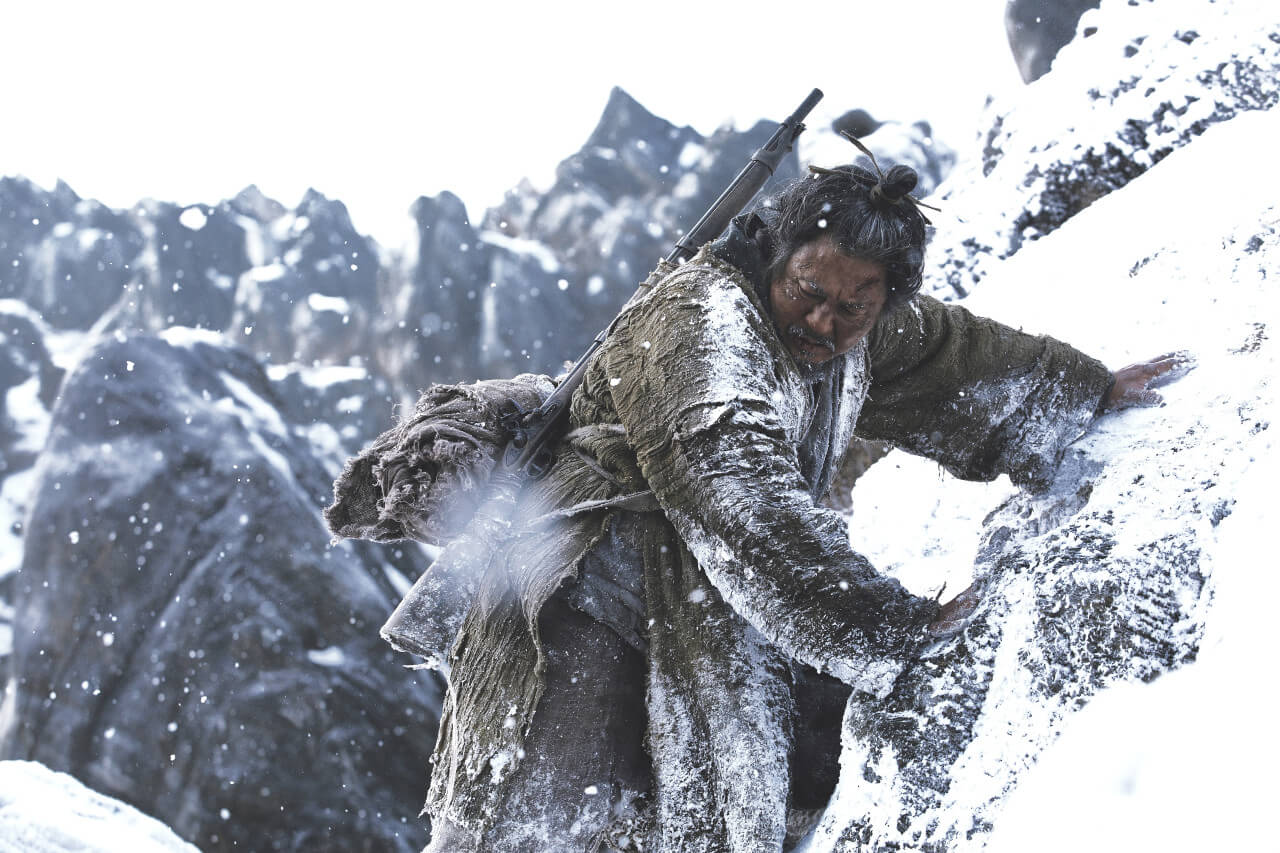 총과 가방을 등에 메고 눈쌓인 산의 절벽을 내려가는 남자