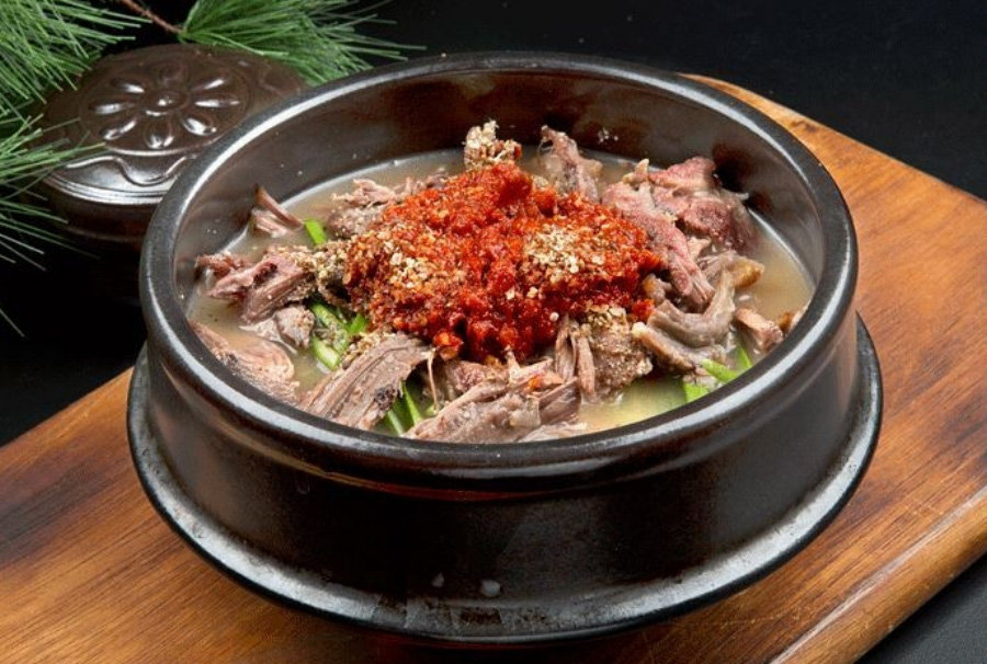 야생에서 채취를 한 개의 살을 넣고 끓여서 만든 개장국, 즉 보신탕을 검은 뚝배기에 가득 담아 놓은 것을 갈색의 나무 깔판 위에 놓아두고 찍은 사진