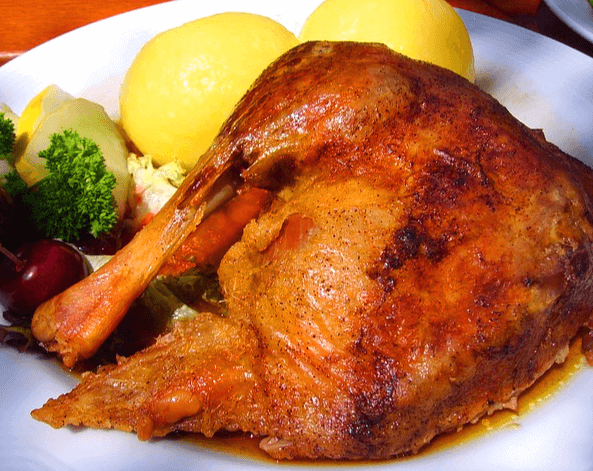 하얀 접시에 거위를 요리한 통구이가 있다. 거위 주변에는 노란 삶은 감자와 초록색 파슬리가 있다.