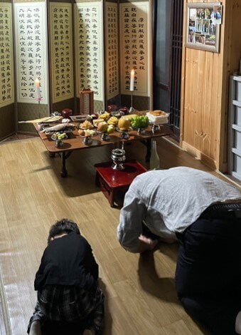 병풍을-뒤로하고-초를-양쪽에-켜둔채로-제사상에-절을하는-모습