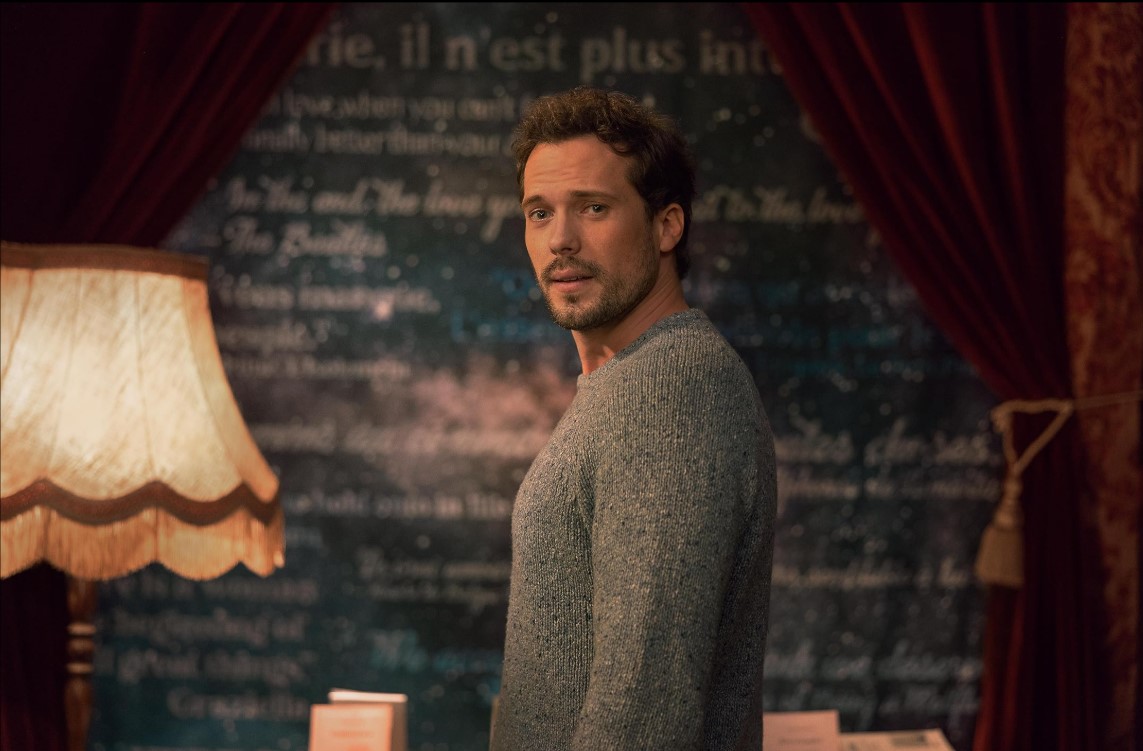 샴페인 프라블럼에서 앙리 카셀 역의 톰 워즈니츠카가 따뜻한 실내에서 뒤돌아보는 장면 – 감성적인 분위기의 캐릭터 스틸컷