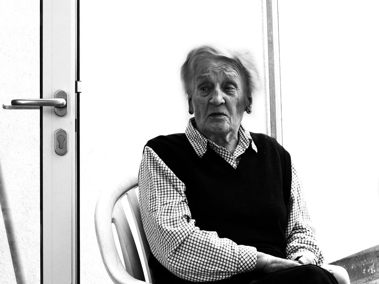 방안에 홀로 의자에 무료한 표정으로 앉아 있는 할머니. 등급 판정을 받아 주간 보호 센터로 보내는 게 도움이 될 수 있음을 암시하는 이미지로 사용