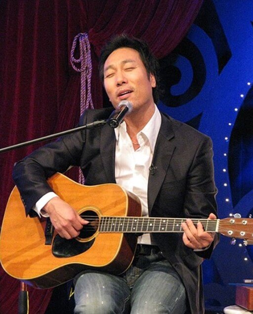 이문세가-무대-의자에-앉아-기타를-치며-노래에-심취해-있는-사진