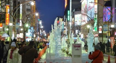 길 한복판에 얼음 조각상이 있고 양옆으로 사람들이 많이 있다.