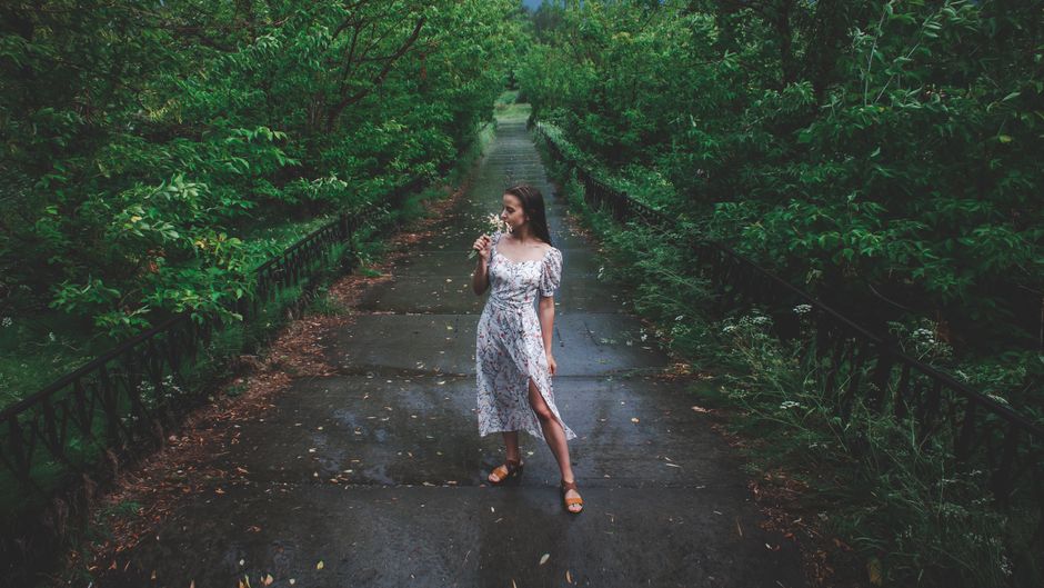 A woman in a floral dress enjoys a walk on a lush green pathway, surrounded by nature.