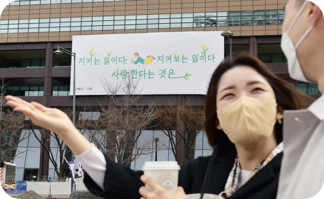 #2021년 광화문글판 봄편 문안 #광화문글판 #허수경 #라일락 #광화문글판 앞에서 손바닥으로 어딘가를 가르키는 마스크 쓴 여자