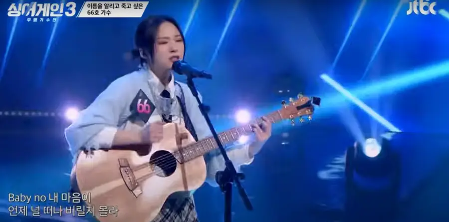 싱어게인3- 하늘색 자켓을 입고 갈색 기타를 치며 스탠딩마이크 앞에서 진지하게 노래하는 66호