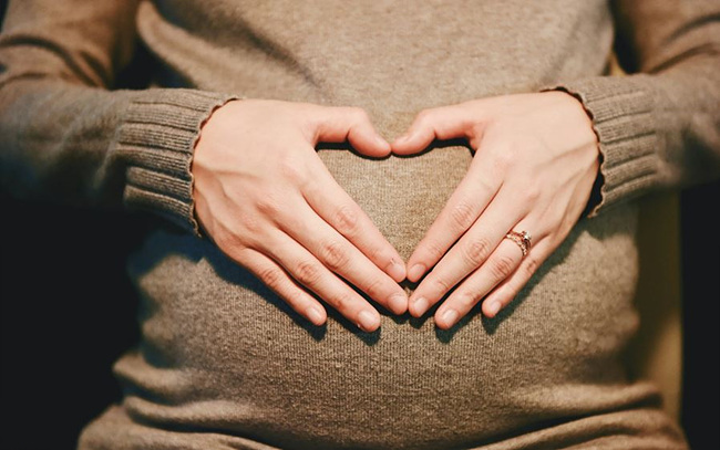 임신한 여성이 배위에 손으로 하트를 만든 사진