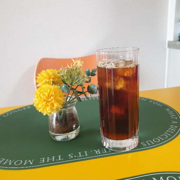 테이블 위에 꽃병. 꽃병 속에는 원두 파우더가 있다. 아이스커피가 담긴 유리잔도 같이 있다.