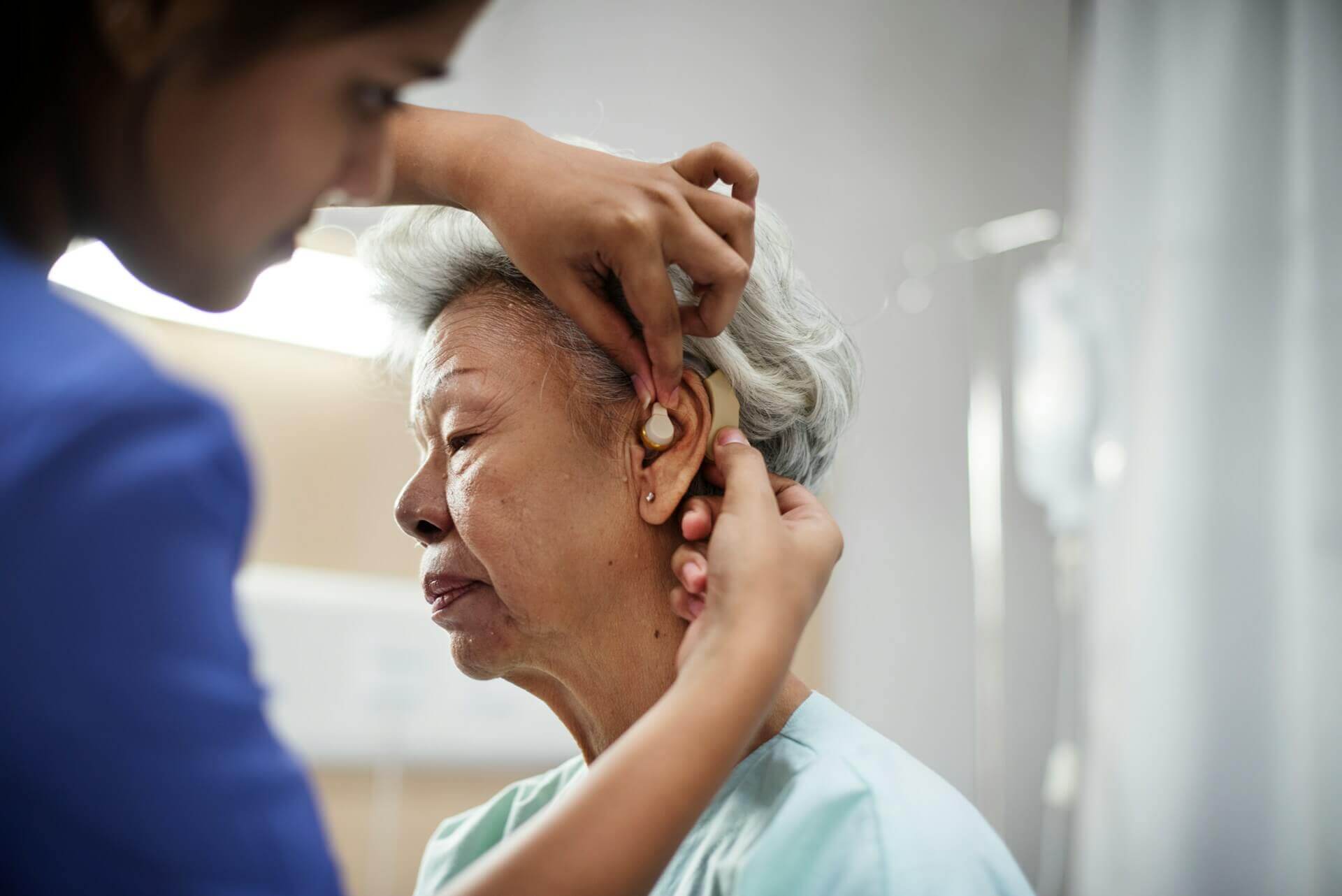 의료인이 고령 여성의 귀에 보청기를 착용해 주는 모습