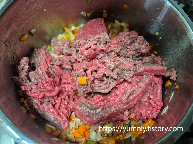 Browning ground beef in a large pot with sautéed vegetables
