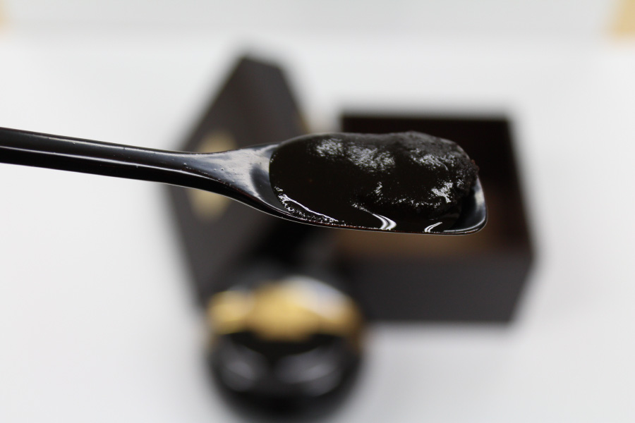 야생에서 채취를 생지황, 인삼, 백복령, 꿀을 한꺼번에 넣고 달여서 만든 경옥고를 담은 단지와 상자를 배경으로 검은 숟가락으로 경옥고를 가득 담은 것을 확대를 하여 찍은 사진