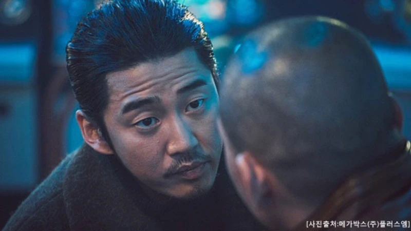 긴 검은머리를 뒤로 묶고 갈색 겨울 코트를 입고 연기하는 영화 범죄도시의 윤계상