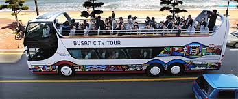 부산 해변 도로를 달리는 2층 시티투어 버스, 관광객들이 바다 풍경을 즐기는 모습.