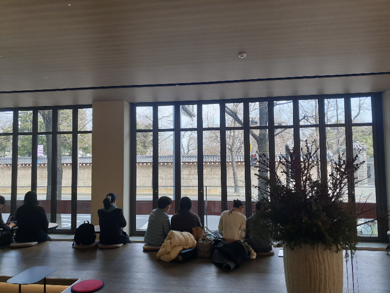 긴 폴딩도어 밖으로 경복궁 담벼락이 보인다. 담을 바라보고 앉은 사람들의 뒷모습