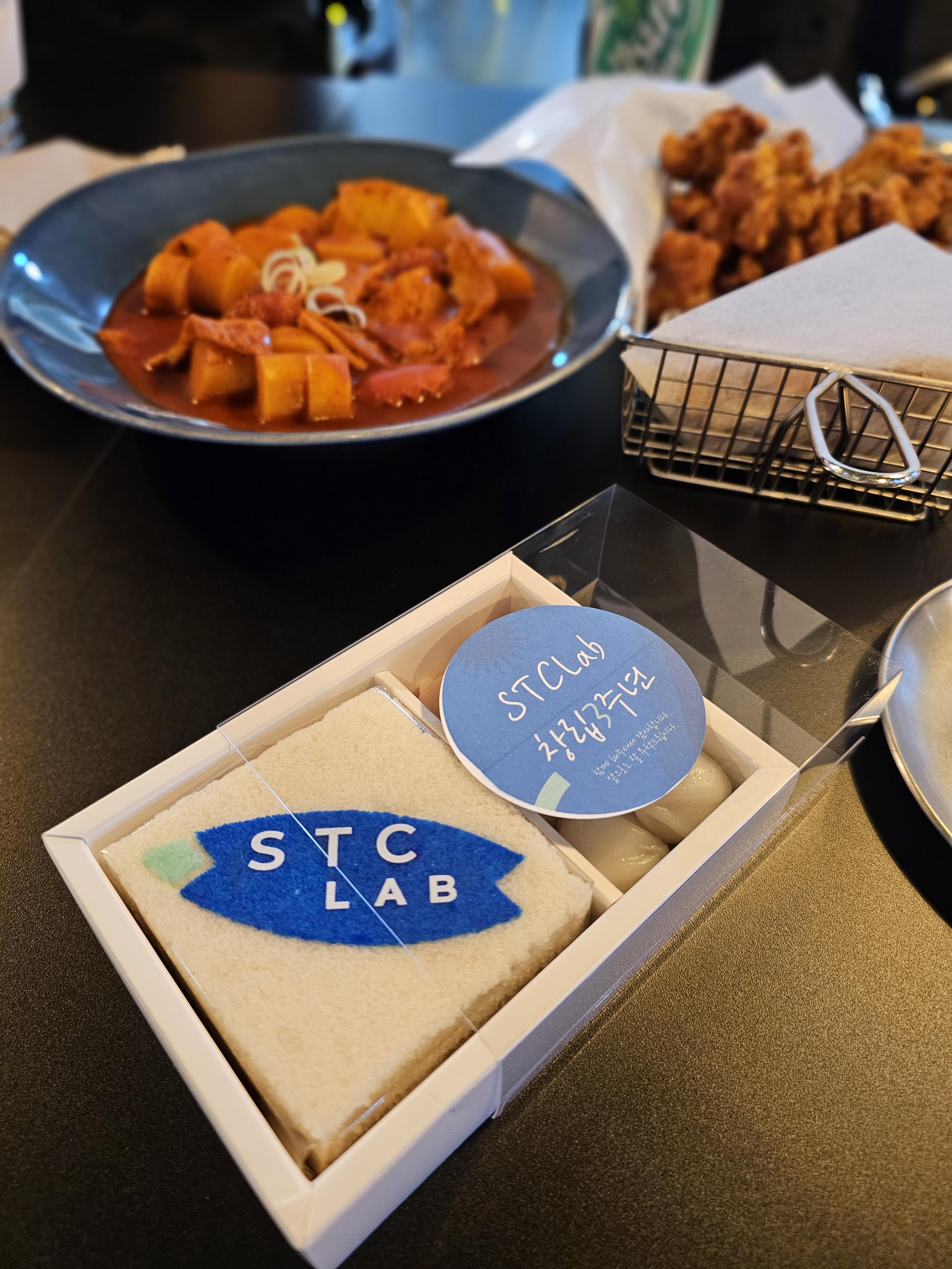 에스티씨랩 로고가 새겨진 떡이 든 상자와 각종 음식들