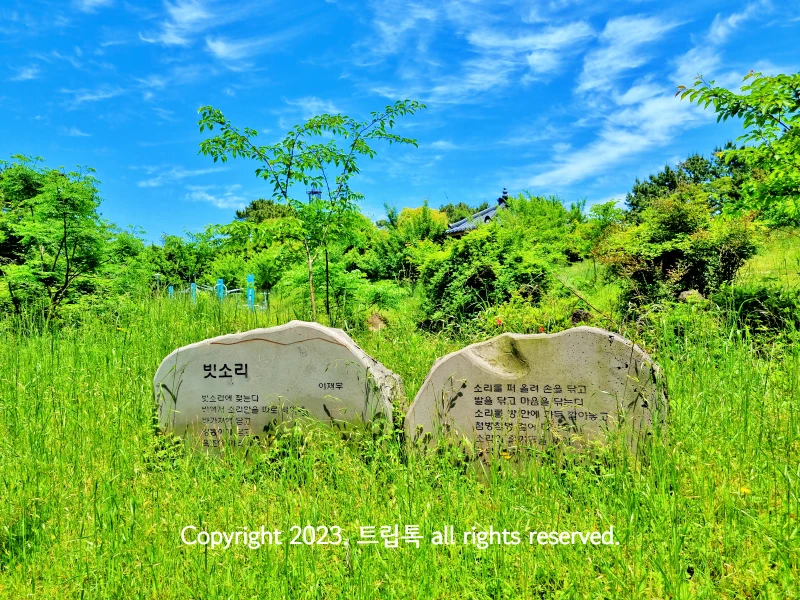 큰 돌을 반으로 잘라서 빗소리라는 시를 적어뒀다. 많은 풀과 하늘이 보인다.