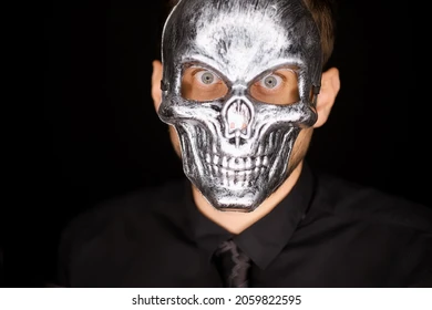 검은옷을 입은 남자가 은색 해골모양의 가면을 쓰고 정면을 바라보는 사진입니다.