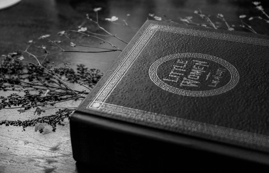 Monochrome close-up of Little Women book on wooden table.