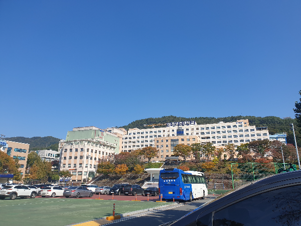 운동장에 차들이 주차되어 있고 운동장 뒤에는 본관 건물이 있다.