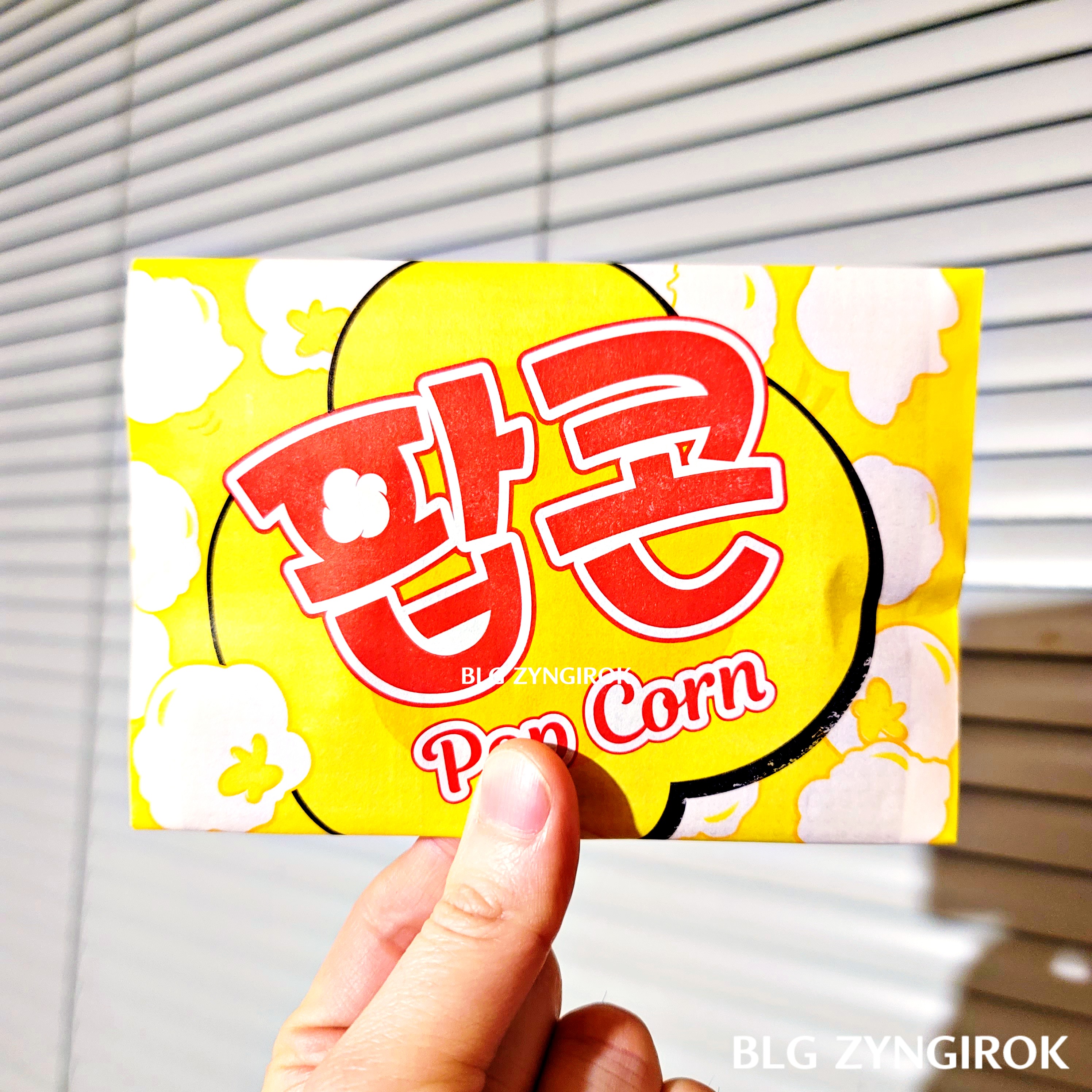 접혀져 있는 노브랜드 팝콘 봉투를 들고있다.