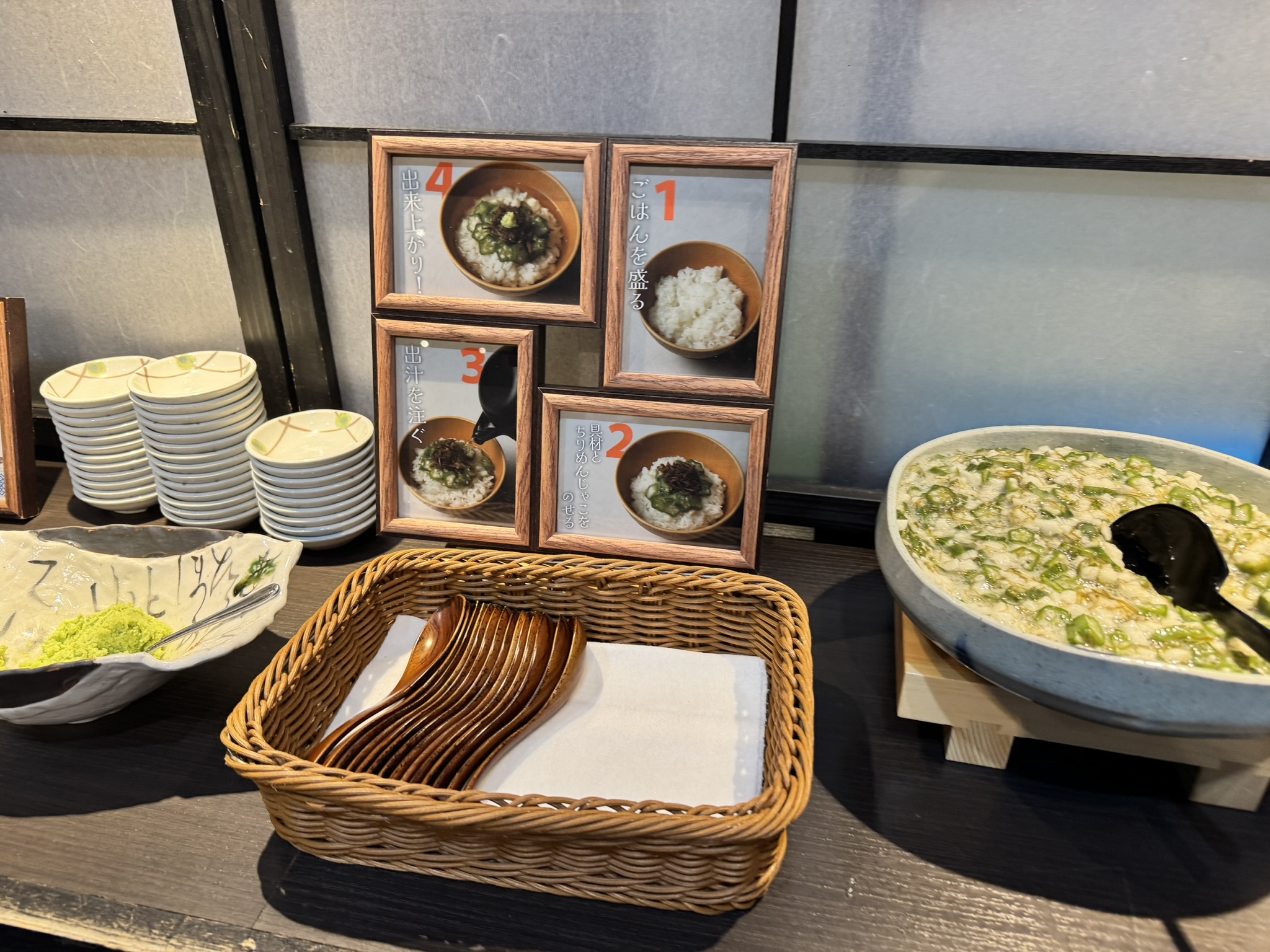 직접 만들어 먹는 '오쿠라 마 덮밥' 코너. 만드는 방법이 1번부터 4번까지 사진으로 설명된 액자가 세워져 있고, 옆에는 잘게 다진 오쿠라와 마 반죽이 담긴 큰 그릇, 나무 숟가락 바구니가 놓인 모습.