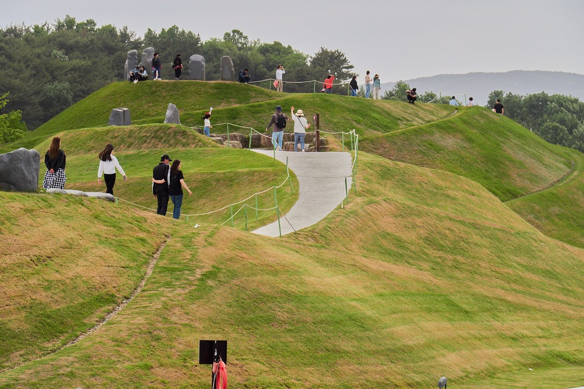 Visitors walking a curving path over grassy mounds at Suncheon Bay National Garden