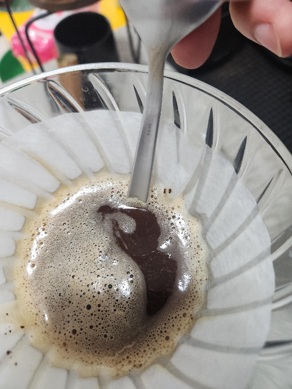 커피 베드를 스푼 뒤로 들어올리는 모습. 커피 배드에 물이 잘 스며들도록 하는 중이다.