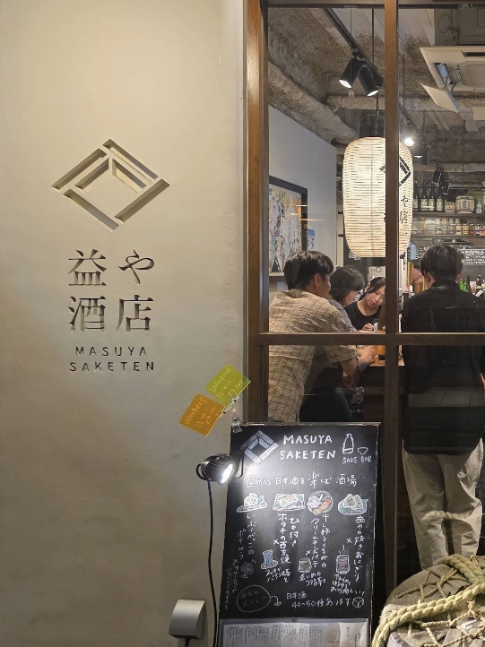 왼쪽 간판이 보이고 창 안쪽 서서 술을 즐기는 사람들이 보인다.