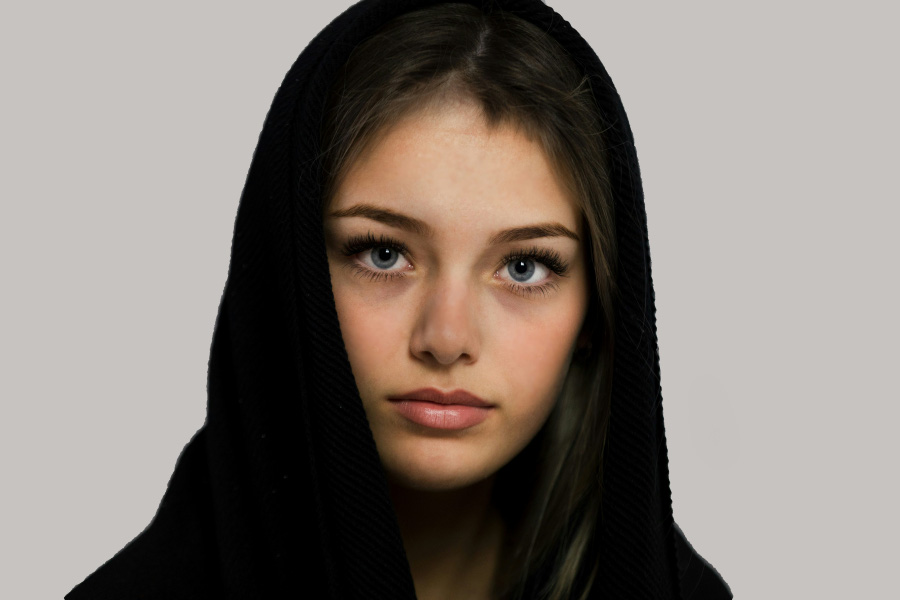 젊은 서양 여성이 무표정으로 정면을 응시하면서 머리에 모자가 달린 검은 윗옷을 입고 찍은 사진