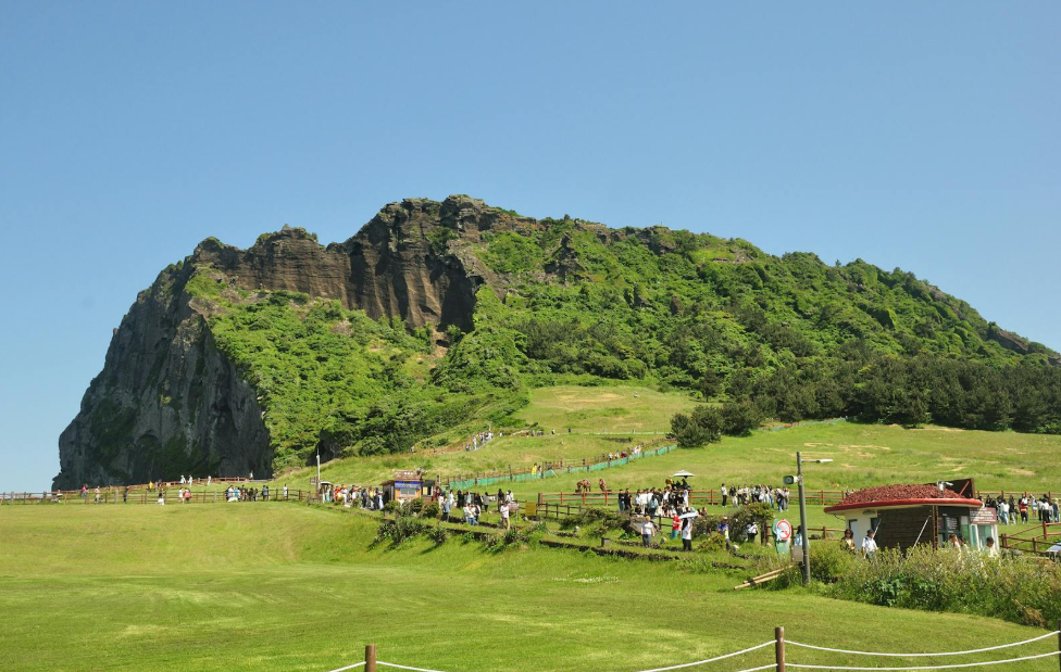 제주도 동쪽 해안에 위치한 수성화산체 성산일출봉 전경. 분화구 주변 초지가 펼쳐져 있고, 많은 관광객들이 트레킹을 즐기고 있는 모습.